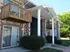 Brick apartment building with white columns and wooden balconies. Sliding glass doors and well-kept shrubs add to a tidy appearance under a clear blue sky.