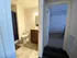 A well-lit bathroom with a toilet and vanity is visible on the left. An adjacent doorway leads to a carpeted room. The atmosphere is clean and simple.