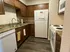 A small kitchen with dark wood cabinets, white appliances including a fridge and stove, granite countertops, and a stylish, warm, and inviting tone.