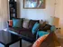 A cozy living room with a dark brown couch adorned with teal and orange pillows. A colorful abstract painting hangs above, creating a warm atmosphere.