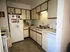 A small, cozy kitchen with white cabinets, a fridge decorated with magnets, a dishwasher, and a sink under warm yellow lighting. Tidy and inviting atmosphere.