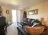 A cozy living room with a large mirror, tan couches adorned with colorful cushions, and a coffee table. Light streams through glass doors onto beige carpet.