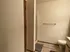 A tidy bathroom with beige walls features a towel rack above a toilet, a shower area, and neatly placed floor mats. Soft lighting creates a calm atmosphere.
