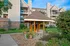 Wooden gazebo with bench seating in a landscaped courtyard at Cobblestone Village, surrounded by flower pots and apartment buildings.