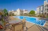 Resort-style swimming pool at Cobblestone Village with poolside seating, shaded tables, and surrounding apartment buildings in a beautifully landscaped setting.