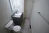 Narrow bathroom featuring a single-sink gray vanity with a marble countertop, lighted mirror above, and a white toilet to the left, with beige tile flooring and a towel bar on the right wall.