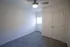 Compact bedroom with light gray carpet, white walls, a window on the left wall, and a closed closet with white double doors; modern ceiling fan with light is mounted on the ceiling.