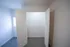 Compact bedroom with light gray carpet, white walls, a window on the left, and an open, well-lit closet with white double doors and metal shelving; modern ceiling fan with light is mounted on the ceiling.