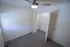 Compact bedroom with light gray carpet, white walls, a window on the left wall, and an open closet with white double doors and a wire shelf; modern ceiling fan with light is mounted on the ceiling.