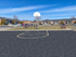 Outdoor basketball court with a single hoop and marked key area, located within a fenced area of the apartment complex surrounded by grass and picnic tables.