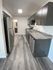 Contemporary galley kitchen with gray wood-look vinyl flooring, dark wood cabinets, stainless steel appliances including a fridge, stove, microwave, and dishwasher, and gray marble-style countertops.