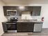 Front-facing view of modern kitchen with double sink, stove, over-the-range microwave, dishwasher, and dark cabinetry set against a neutral wall; a fire extinguisher is mounted on the wall.