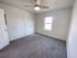 Carpeted bedroom with ceiling fan, single window, and a wide double-door closet, offering a simple, bright layout with neutral colors.