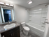 Modern bathroom with white acrylic bathtub and shower combo featuring built-in shelves, a toilet, and single-sink vanity with dark wood cabinet and backlit mirror.