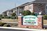Brick entrance sign with green and white lettering that reads &ldquo;Delaware on Primrose&rdquo; with contact information and address, positioned in front of the apartment complex.