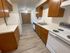 Galley kitchen featuring wood cabinetry, white countertops, white appliances including stove and refrigerator, and vinyl plank flooring; open view into adjacent dining area.
