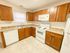 Bright kitchen with warm wood cabinets, white appliances, and beige countertops. The room feels clean and inviting, with natural light from a window.