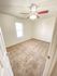 Empty room with beige carpet, white walls, and a ceiling fan with lights. A single window allows natural light, creating a bright, clean atmosphere.