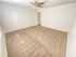 Spacious empty room with beige carpet, white walls, and a ceiling fan. Two closed doors; sunlight streams through a window, creating a serene atmosphere.