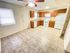 A bright, empty kitchen with wood cabinets, white appliances, and beige tile flooring. A ceiling fan is above, adding a welcoming and clean atmosphere.
