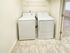 A well-lit laundry room with a white washing machine and dryer side by side on a tiled floor. Shelving is above, creating a clean, streamlined look.