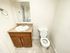 Simple bathroom with beige walls and tiled floor. Features a wooden vanity with a marble countertop and a sink on the left, and a white toilet on the right.