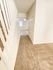Bright hallway in a modern home with beige tiled floors, white walls, and a staircase on the left. The corridor leads to a room with natural light.