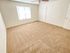 Empty room with beige carpet and white walls, featuring a large window with blinds and a white door. The room feels bright and spacious with a modern ceiling fan.