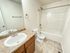 A clean bathroom with a white bathtub-shower combo, toilet, and sink. Marble countertop, wooden cabinet, mirror, and neutral tiles create a fresh tone.