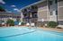 View of a clean, blue swimming pool surrounded by lounge chairs, with a multi-story apartment building in the background under a clear sky.