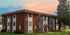 El Madrid Apartments exterior at sunset &ndash; Three-story red brick apartment building with white accents, small balconies, and a red tile-style roof, set against a colorful sunset sky.