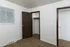 Empty bedroom with brown carpet, white walls, a small window, and an open closet with dark wood doors.
