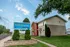 A beige and red two-story townhome under a blue sky, with a "The Townhomes at Quail Ridge" sign in front, surrounded by trimmed hedges and a tree, conveys a welcoming suburban feel.