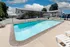 Outdoor pool at a motel with clear blue water under a partly cloudy sky. The motel's two-story building is in the background. Relaxed, sunny atmosphere.