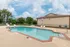 Outdoor pool framed by red brick and cream siding, with poolside seating and mature landscaping in a secure, fenced area.