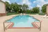 Rectangular outdoor pool with red brick trim, surrounded by concrete decking and lush trees in the background&mdash;perfect for relaxing summer days.