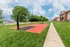Red and black basketball court with dual hoops, surrounded by lush grass and a sidewalk&mdash;perfect for recreation.