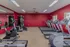 Quail Ridge Apartments fitness center featuring treadmills, stationary bikes, and strength training equipment. The room includes red walls, large mirrors for visibility, and natural light from multiple windows. The layout provides clear pathways for accessibility, ensuring an inclusive and welcoming workout space for all residents.
