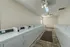 Quail Ridge Apartments laundry room with two rows of white commercial washers and dryers, separated by a central walkway with a non-slip rug for safety. The room features beige walls, overhead lighting, ceiling fans, and a skylight for natural illumination. The layout provides wide, clear pathways for easy accessibility.
