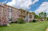 Exterior view of Grandview Apartments featuring brick and siding buildings with private wooden balconies. The well-maintained lawn, trimmed bushes, and mature trees provide a serene setting under a partly cloudy blue sky.