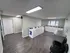 A clean, modern laundry room featuring several top-loading washing machines and front-loading dryers against light green walls. The room has tiled floors in a dark gray tone, a window for natural light, and a small seating area with black chairs.