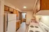 A well-lit kitchen with wooden cabinets, a white stove, and a refrigerator. A small hallway leads to a bathroom vanity with a large mirror.