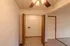 A designated laundry space with open wooden folding doors, featuring washer and dryer hookups, a white wire shelf, and beige wood-style flooring.