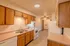 A long galley-style kitchen with wooden cabinets, a white electric stove, a dishwasher, and a double sink. A fire extinguisher is mounted on the wall near the laundry closet.