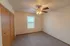 A bedroom with neutral-colored carpet, a ceiling fan with lights, a window with blinds, and a large wooden closet with sliding doors.