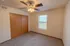 A cozy bedroom with a built-in double-door closet, beige carpet, a window with blinds, and a ceiling fan with wooden blades.