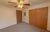 A well-lit bedroom featuring a ceiling fan with lights, a large closet with wooden sliding doors, and a secondary closet door leading to the kitchen and bathroom area.