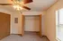 A bedroom with an open double-door closet, showcasing a built-in white wire shelf for storage. The room has beige carpet and a window with blinds.