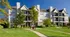 Exterior view of Cobblestone Village Apartments featuring three-story buildings with private balconies, mature trees, and well-maintained green spaces.