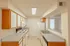 Galley-style kitchen with white appliances including an electric stove, microwave, refrigerator, and dishwasher, along with laminate countertops, wood-trimmed cabinetry, and overhead fluorescent lighting.